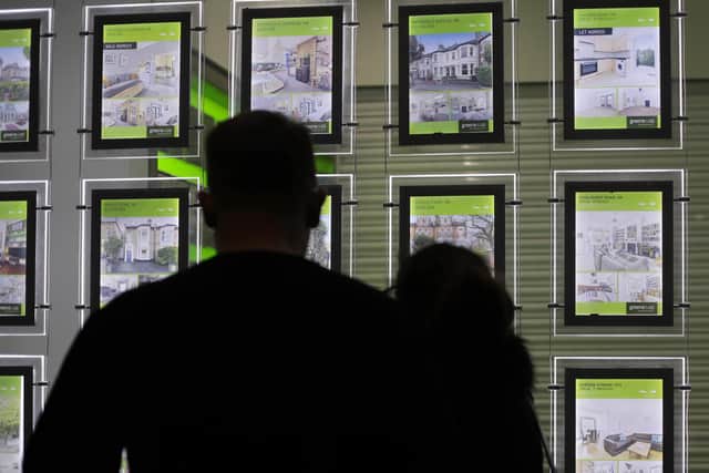 Library image of people looking at homes for sale in an estate agent's window,
