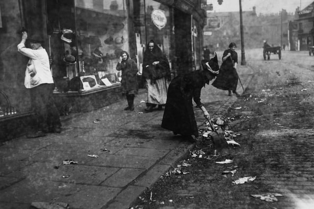 Shopkeepers sweeping up and removing rubbish from the roadway outside their premises during the Leeds municipal workers strike.