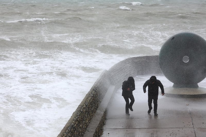 People walk on on a sea wall at high tide.