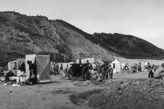 Children building a sand mound with a moat and adults relaxing by their changing tents on the beach at Filey.
