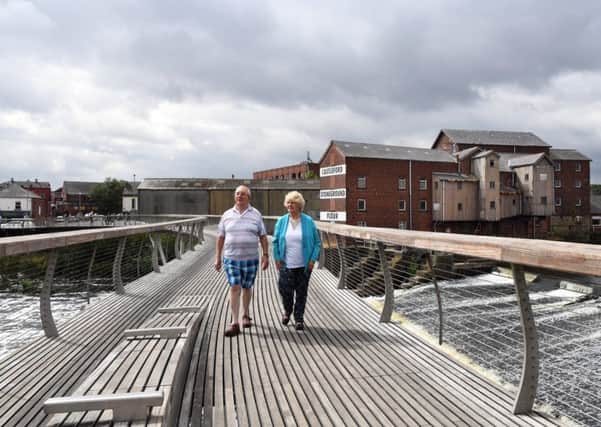 Alison Drake and Rod Rayner walk across the Millennium Bridge with Queen's Mill in the bsckground. 14th August 2018.
