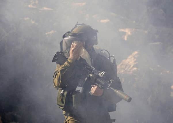 An Israeli army soldier covers his face for protection as he walks through during clashes with Palestinian protesters. When will the bloodshed in the Middle East be halted?