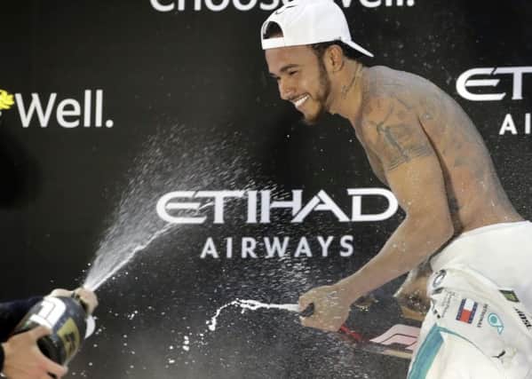 Mercedes driver Lewis Hamilton of Britain spays rose water celebrating his victory on the podium of the Emirates Formula One Grand Prix at the Yas Marina racetrack in Abu Dhabi.(AP Photo/Luca Bruno)