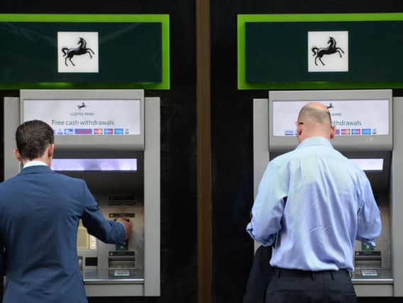 Bank customers use a cash machine. A committee of MPs has called for Minister to force banks to keep a branch open in every UK town.