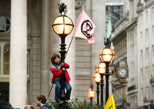 A young protester standing on a lamp post, in front of The Royal Exchange, London, during an Extinction Rebellion (XR) climate change protest. PA Photo. Picture date: Monday October 14, 2019. See PA story ENVIRONMENT Protests. Photo credit should read: Jonathan Brady/PA Wire