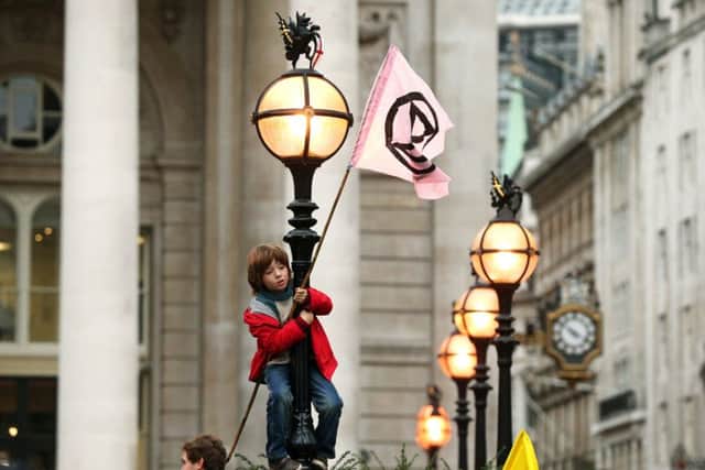 A young protester standing on a lamp post, in front of The Royal Exchange, London, during an Extinction Rebellion (XR) climate change protest.