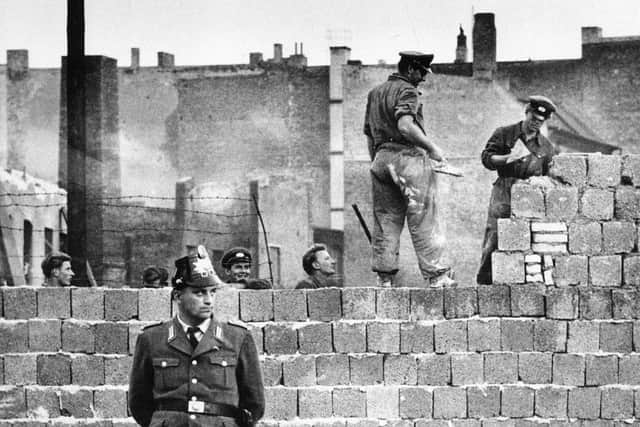 A West Berlin policeman stands in front of the concrete wall dividing East and West Berlin as workmen add blocks to increase the height of the East German barrierin October 1961.