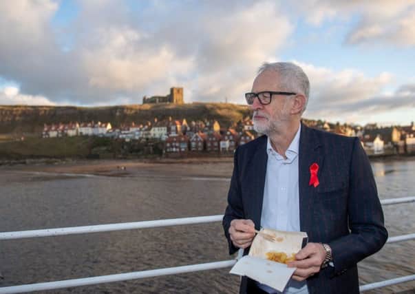 Labour leader Jeremy Corbyn eats chips in Whitby, while on the General Election campaign trail, wearing a jacket that has "for the many not the few" printed all over it.