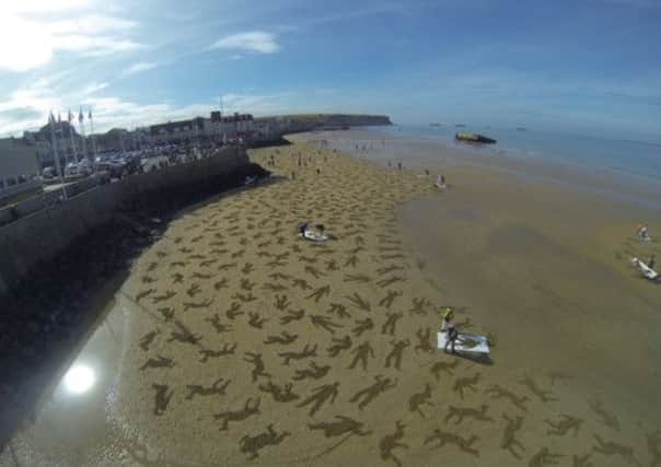 The sun shines on The Fallen, a massive sand art project on the beach of Arromanches, France, for Peace Day 2013