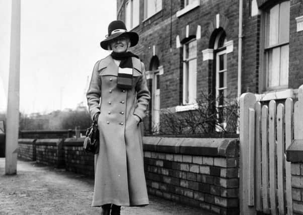 Viv Nicholson wearing a smart camel coloured maxi coat and wide brimmed royal blue hat, that are to be auctioned
