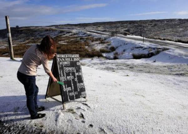 A woman beats the freeze as she clears the snow off signs for the Tan Hill Inn, on the Pennine tops above Reeth in Swaledale