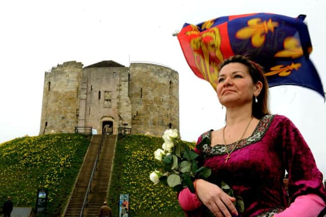 Vanessa Roe, 16th great  niece of King Richard III, clutching white roses in front of a Royal Standard from the Plantaganet period  outside Clifford's Tower in York