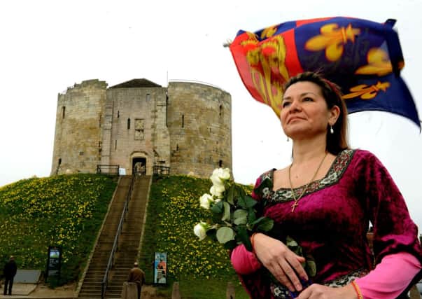 Vanessa Roe, 16th great  niece of King Richard III, clutching white roses in front of a Royal Standard from the Plantaganet period  outside Clifford's Tower in York