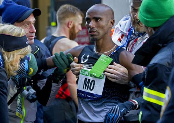 After collapsing at the finish line, Mo Farah of Great Britain is brought to his feet during the 2014 NYC Half marathon.