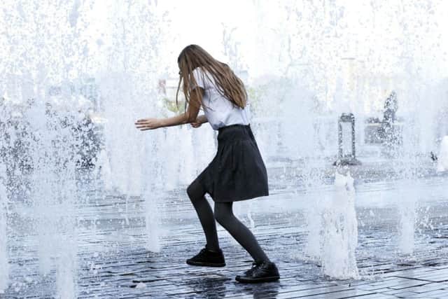 A schoolgirl runs through a fountain to keep cool