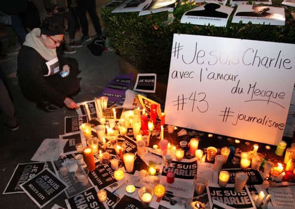 A woman lights a candle on a makeshift alter including signs that read in French "I am Charlie" during a vigil in solidarity with those killed in an attack at the Paris offices of the weekly newspaper Charlie Hebdo
