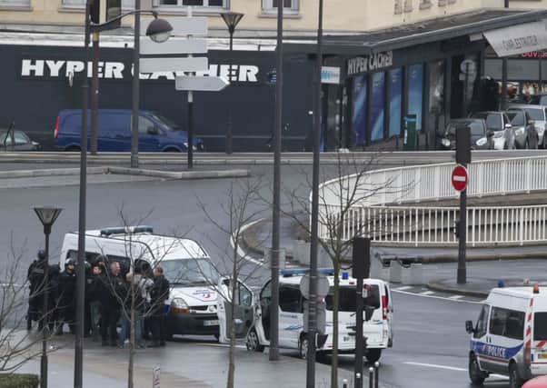 French police officers gather near a hostage-taking situation at a kosher market, visible in the background, in Paris
