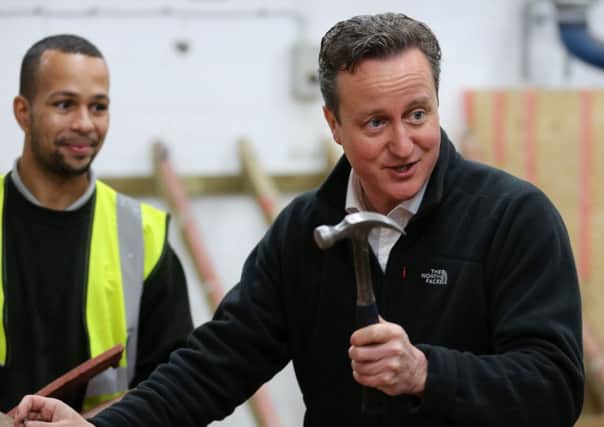 David Cameron fixes tiles to a roof mockup, alongside former roofing apprentice Lynden Blackwood, during a visit to J Wright roofing college in Nottingham.