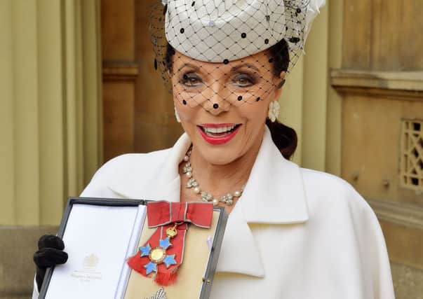 Dame Joan Collins holds her insignia of Dame Commander of the British Empire