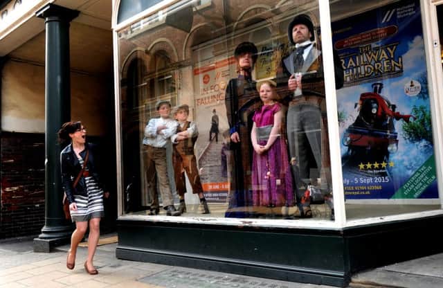 A member of the public has a double take as she sees members of the cast of Fog and Falling Snow standing  in the window of Robson and Coopers in Lendal, York.