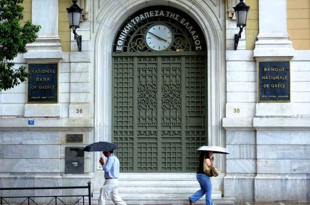 A man and a woman pass outside of the an office of National Bank of Greece in Athens. AP Photo/Petros Karadjias)