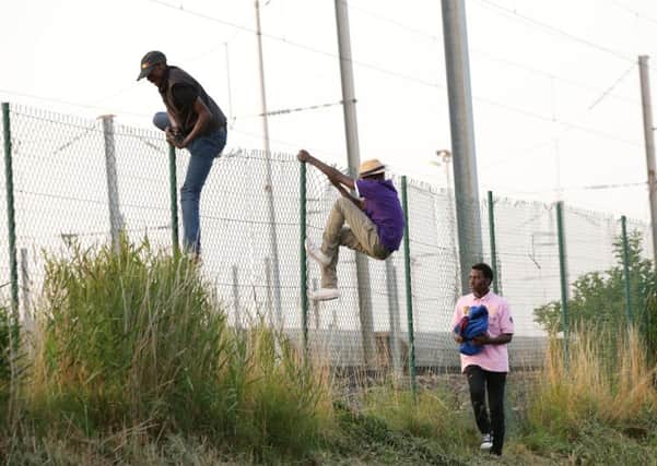 Migrants climb over a fence on to the tracks near the Eurotunnel site at Coquelles in Calais