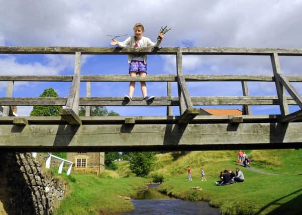 FAMILY FUN: Kirsten Whatley-Bell, from Doncaster, playing Poohsticks on the bridge at Hutton-le-Hole in North Yorkshire, as advice on the perfect stick was published by scientists. PIC: Gary Longbottom