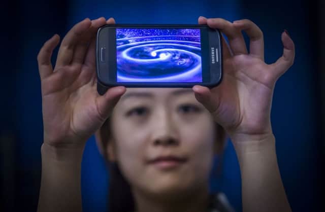 Student Muzi Li at the Institute of Gravitational Research at Glasgow University holding a phone that shows a computer simulation of gravity waves - ripples in spacetime - which have been detected by scientists a century after Albert Einstein predicted their existence.