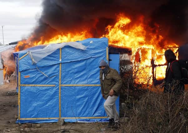 Migrants run past burning tents in a makeshift camp near Calais. Under the eye of hundreds of riot police, workers began pulling down tents and makeshift shelters in the sprawling camp in Calais on Monday, dismantling the fragile structures that have served as temporary homes for migrants hoping to make their way to a better life in Britain.