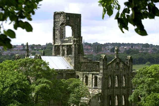 Sunlight strikes  Kirkstall Abbey  which stands in the  suburbs  of Leeds with red brick houses  surrounding the ancient monument .