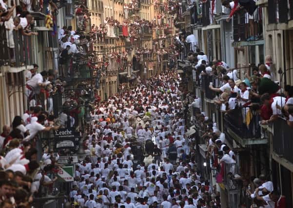 Revelers go on the way of the Estafeta street beside Fuente Ymbro fighting bulls as people look on from balconies during the first running of the bulls at the San Fermin Festival, in Pamplona. (AP Photo/Alvaro Barrientos)