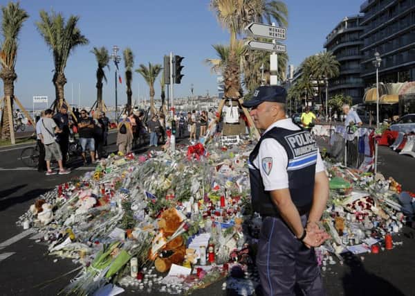 A police officer watches people gathering around a floral tribute for the victims killed during a deadly attack, on the famed Boulevard des Anglais in Nice. PIC: PA