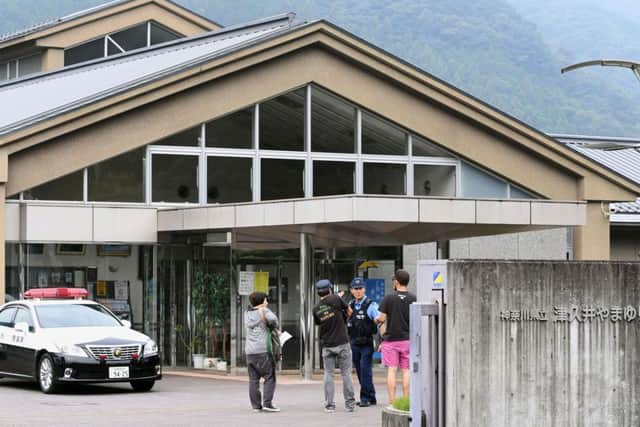 A police officer talks with visitors in front of the facility. (Kyodo News via AP)