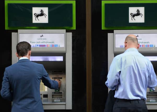 Members of the public using cash machines at a branch of Lloyds Bank in the City of London, as Lloyds Banking Group said it is cutting 3,000 jobs and shutting 200 branches as the lender braces for a cut in interest rates following Britain's decision to quit the European Union.