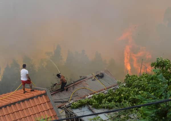 Men spray water on the roofs of houses to protect them from an approaching fire in Curral dos Romeiros, on the outskirts of Funchal, on the Madeira island, Portugal, Tuesday, Aug. 9 2016. Flames from forest fires licked at homes around Funchal, casting a smoke plume over the downtown and forcing the evacuation of more than 400 people. (AP Photo/Helder Santos)