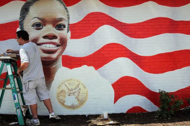 Eric Lindbergh of T.A.L.E.N.T. Murals works on the image of gymnast Gabby Douglas on the side of the Gator's Sports Bar & Grill on Holland Road in Virginia Beach, Va.  on Thursday, Aug.  9, 2012.  The mural shows Douglas holding a gold medal with an American flag backdrop. It says "Way to go Gabby." (AP Photo/Virginian-Pilot, Steve Earley)  MAGS OUT