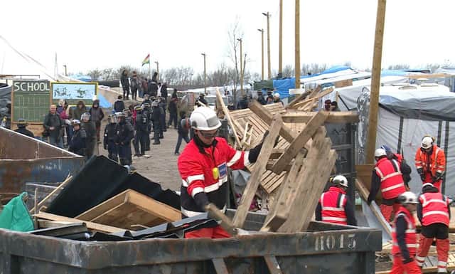 Police officers safeguard helmeted workers pulling down makeshift structures where migrants sleep in the southern sector of the camp near Calais, earlier this year.