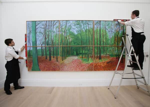 Members of staff at Sotheby's in London attend to David Hockney's painting Woldgate Woods, expected to fetch up to 12 million dollars when it goes under the hammer