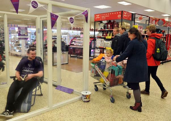 171116    Andrew Robertson begins his 50 hour stay in a perspex box  in the foyer of the Tesco Extra store  on Tadcaster Road in York in  aid  of Locked in for Autism as Shopper Lynda Armstrong and her daughter Cristina 2 (correct) from York walk by.