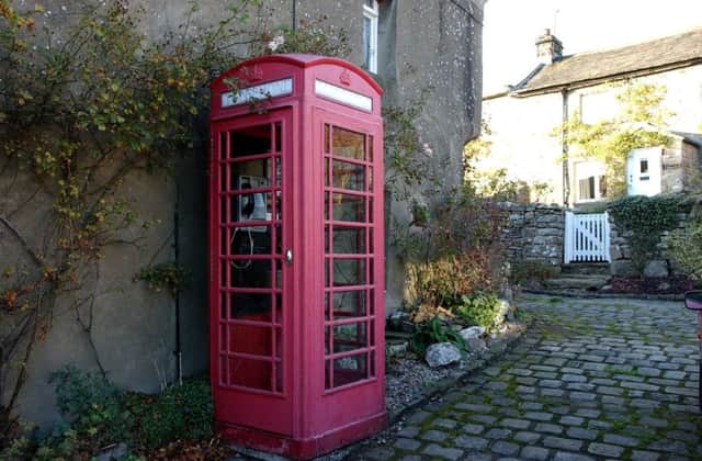 The telephone box in Healaugh, near Reeth, in Swaledale, has vase of flowers, a waste paper bin and carpet on the floor