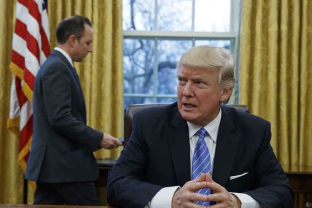 President Donald Trump sits at his desk as he waits for White House Chief of Staff Reince Priebus, left, to deliver three executive orders for his signature, Monday, Jan. 23, 2017, in the Oval Office of the White House in Washington. (AP Photo/Evan Vucci)