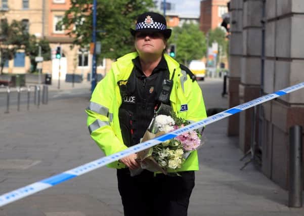 A police officer moves a floral tribute close to the Manchester Arena, the morning after a suicide bomber killed 22 people, including children, as an explosion tore through fans leaving a pop concert in Manchester. PIC: PA