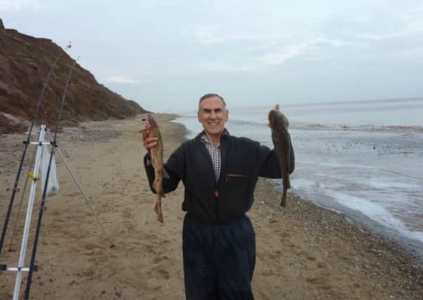 Stewart Calligan holds aloft a lesser spotted dogfish and a cod during a wet day at the beach.