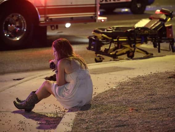 A woman sits on a curb at the scene of a shooting outside of a music festival along the Las Vegas Strip. More than 50 people are confirmed to have been killed in the shooting. (AP Photo/John Locher)
