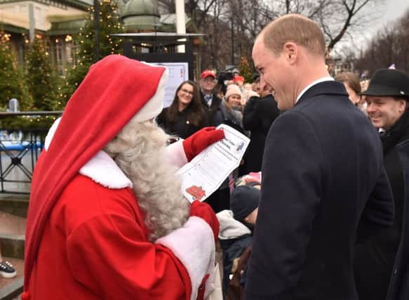 The Duke of Cambridge hands Prince George's Christmas Wish List to a man dressed as Santa Claus as he visits Esplanade Park's Christmas market in Helsinki, on the second day of his tour of Finland.