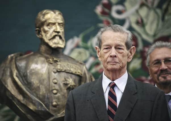 King Michael poses next to a bronze sculpture depicting the founder of Romania's royal dynasty, King Carol I, in the country's parliament in Bucharest