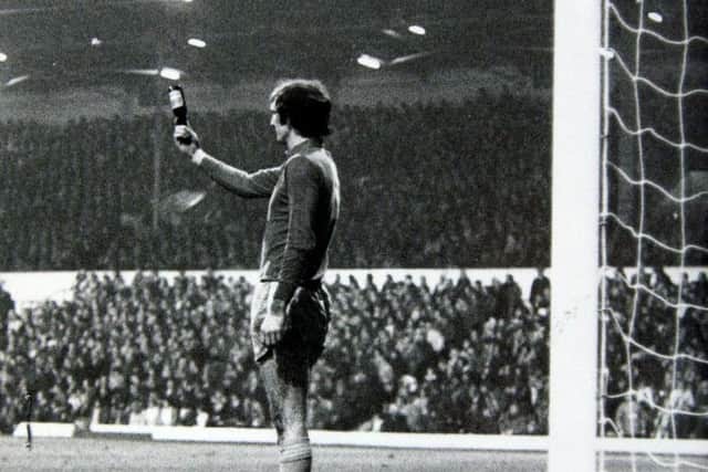 Manchester City goalkeeper Joe Corrigan holds up a bottle which was thrown at him from the Kop