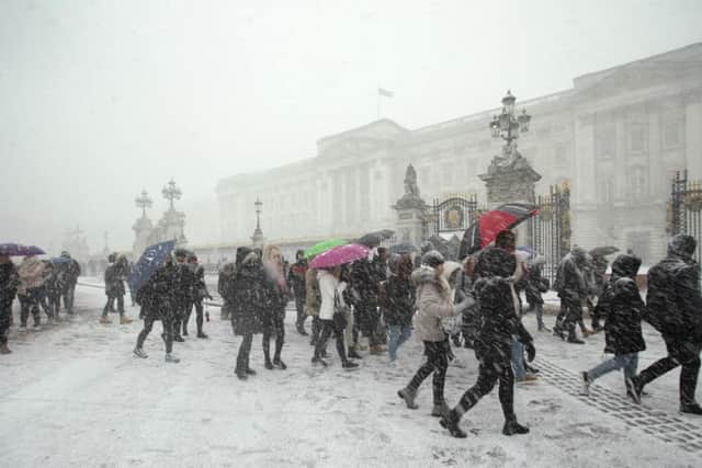 People walk past Buckingham Palace, in London, in the snow, as heavy snowfall is affecting roads across the UK. PA